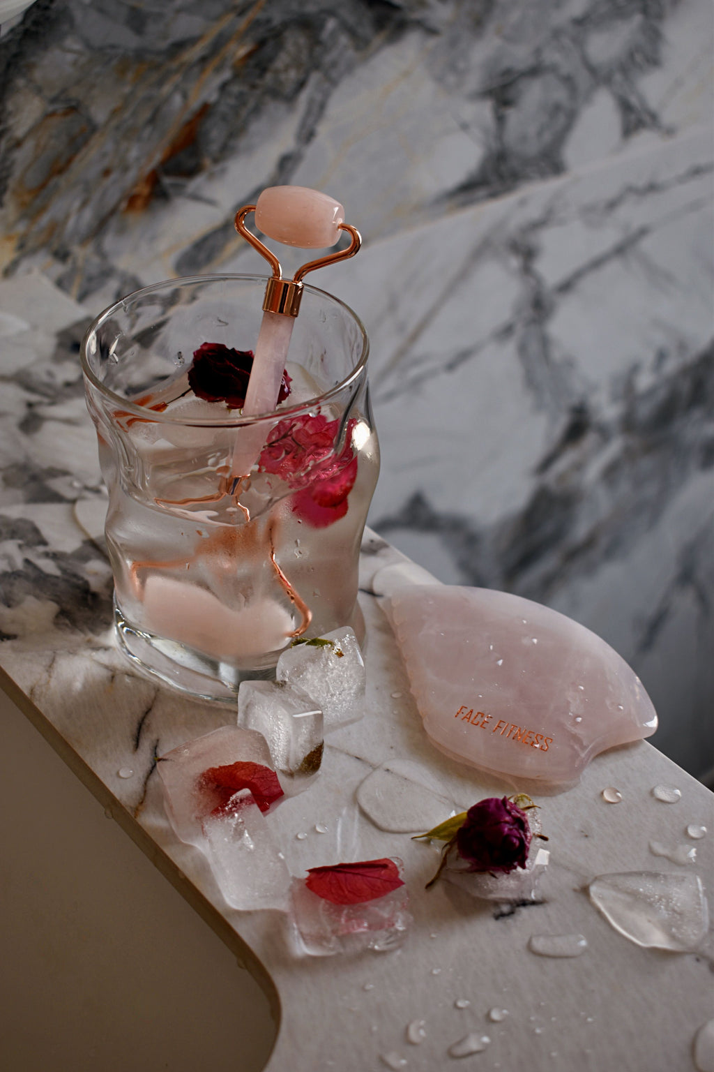 Rose quartz skincare tools with rose petals and ice on marble
