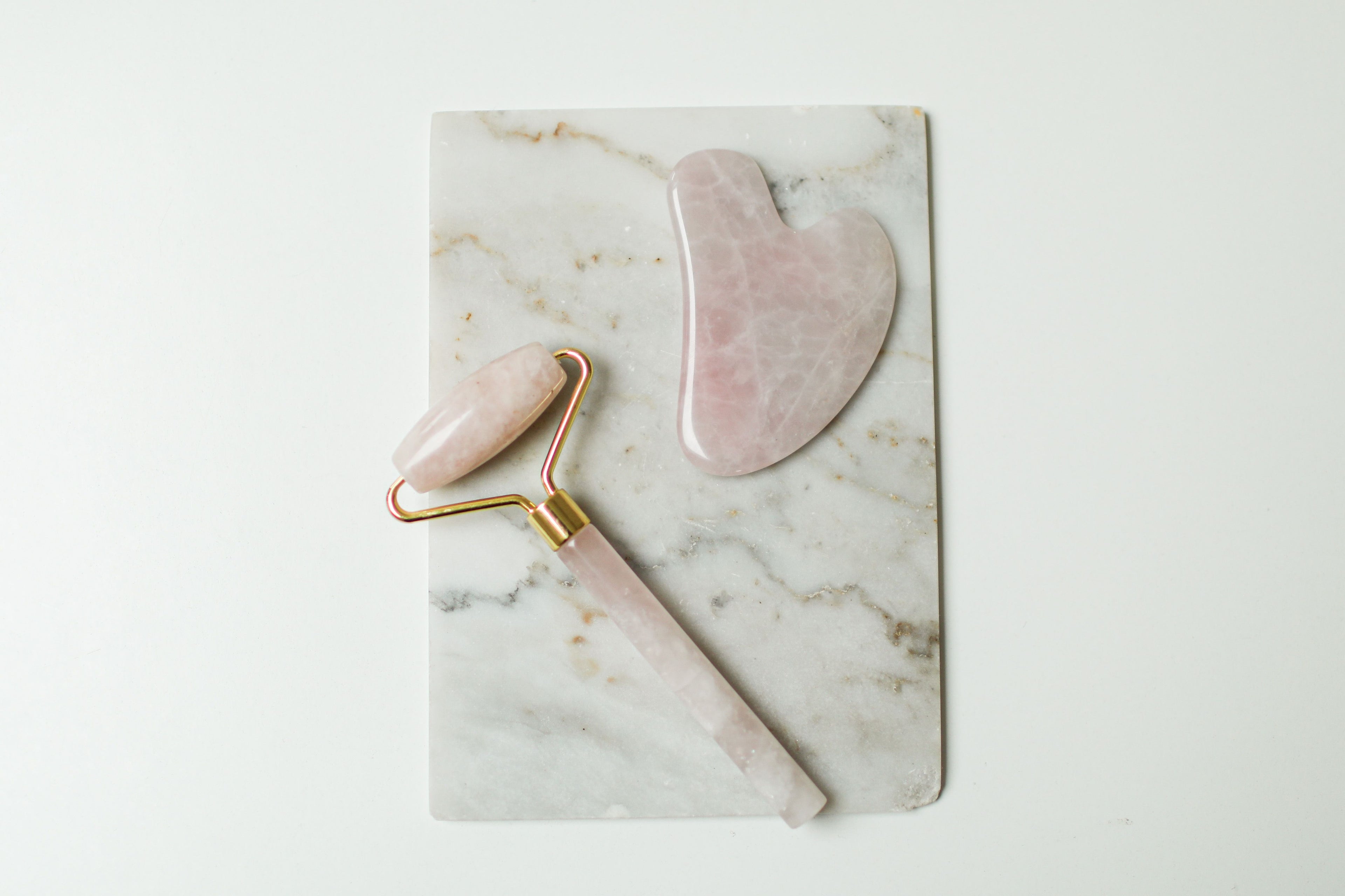 Sielvane rose quartz facial roller and gua sha stone flat lay on marble